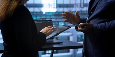 Hände von einer Frau und einem Mann, die jeweils technische Geräte halten und miteinander sprechen